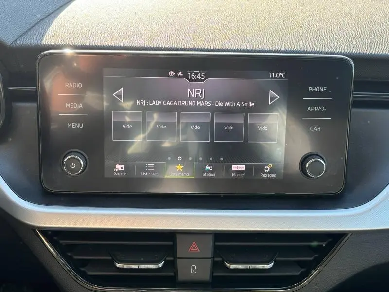 Écran tactile central du Skoda Kamiq 2023 affichant la radio NRJ avec commandes latérales et tableau de bord noir.