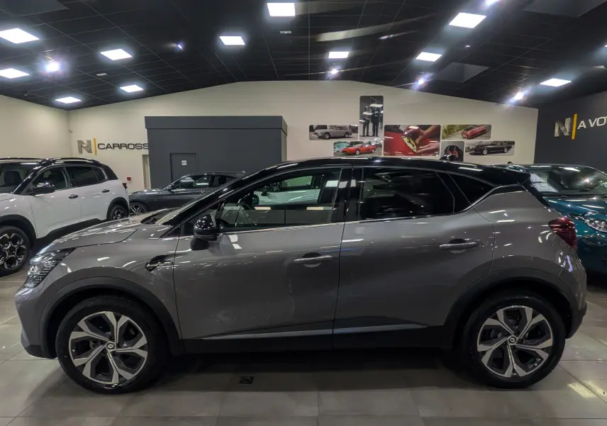 Profil côté gauche du Renault Captur TCe 160 R.S. Line 2022 en gris Cassiopé avec toit noir dans un showroom.
