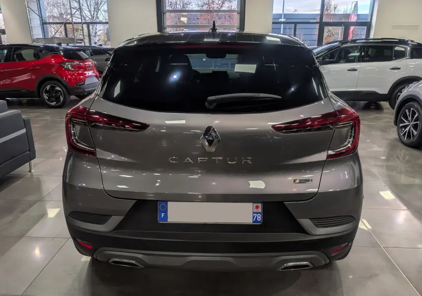 Vue arrière d'un Renault Captur gris Cassiopé avec toit noir, en intérieur, mettant en valeur son badge hybride et ses feux LED fins.