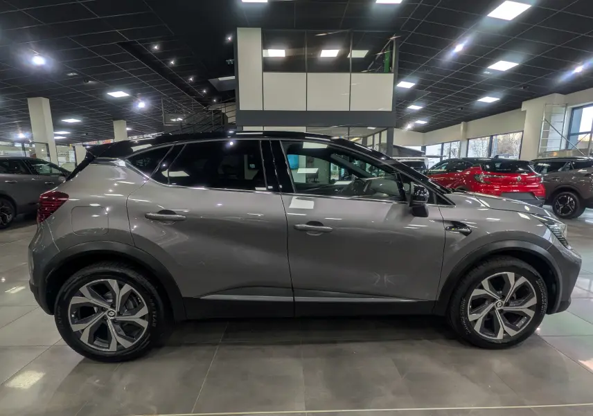Profil droit d'un Renault Captur TCe 160 R.S. Line 2022 gris Cassiopé avec toit noir en showroom lumineux.