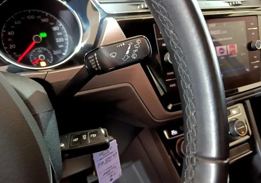 Gros plan sur le volant cuir et la commande d'essuie-glace du Volkswagen Touran 1.5 TSI bleu, tableau de bord et écran tactile visibles.