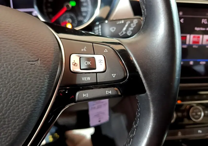 Gros plan sur les commandes au volant cuir côté gauche du Volkswagen Touran bleu, avec tableau de bord et écran tactile en arrière-plan.