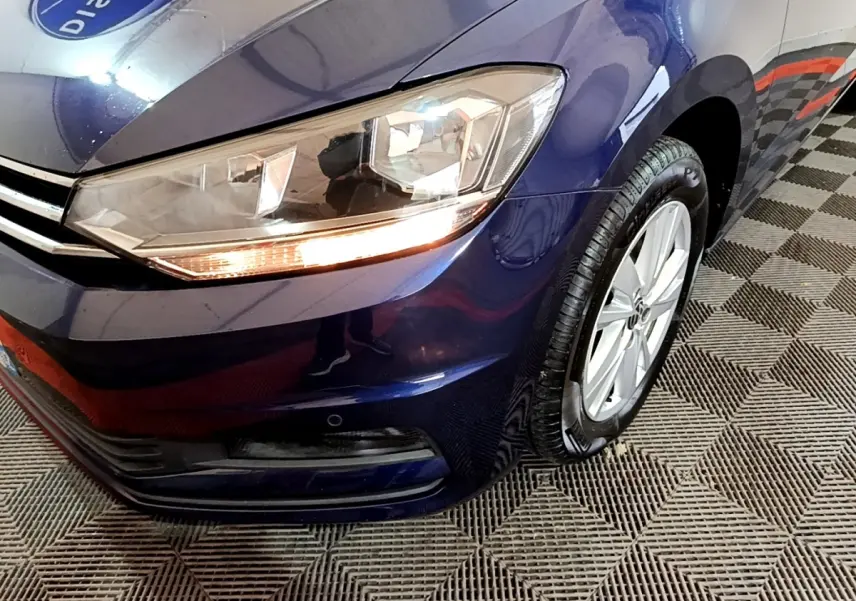 Gros plan sur l'avant droit bleu d'un Volkswagen Touran 1.5 TSI EVO DSG7 avec phare allumé et jante alliage.
