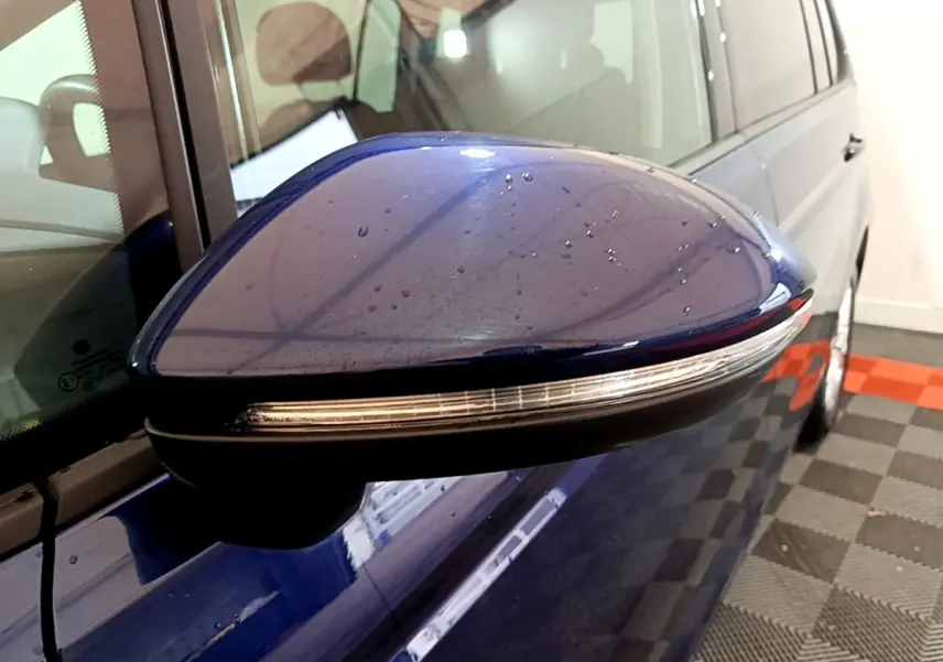Rétroviseur côté gauche bleu du Volkswagen Touran 2021 avec clignotant intégré, vue rapprochée en intérieur.