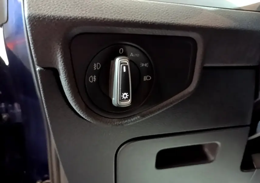 Gros plan sur le sélecteur des phares noir dans l'habitacle du Volkswagen Touran bleu, côté gauche conducteur.