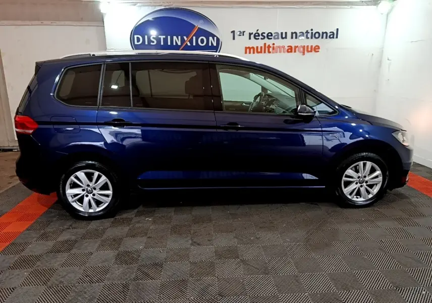 Profil droit d'un Volkswagen Touran bleu 2021 garé en intérieur avec vitres teintées et jantes alliage.