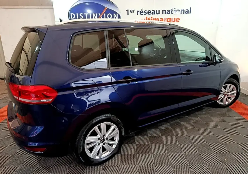 Vue côté droit arrière d'un Volkswagen Touran bleu 2021 garé en intérieur sur sol damier noir et rouge.