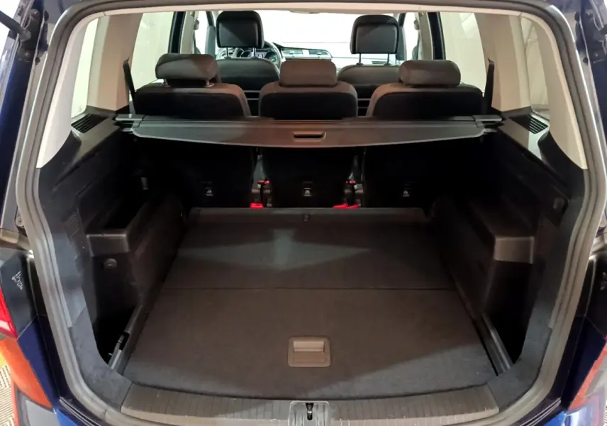 Vue arrière du coffre ouvert du Volkswagen Touran bleu 1.5 TSI EVO DSG7 United avec banquette arrière et cache-bagages visibles.
