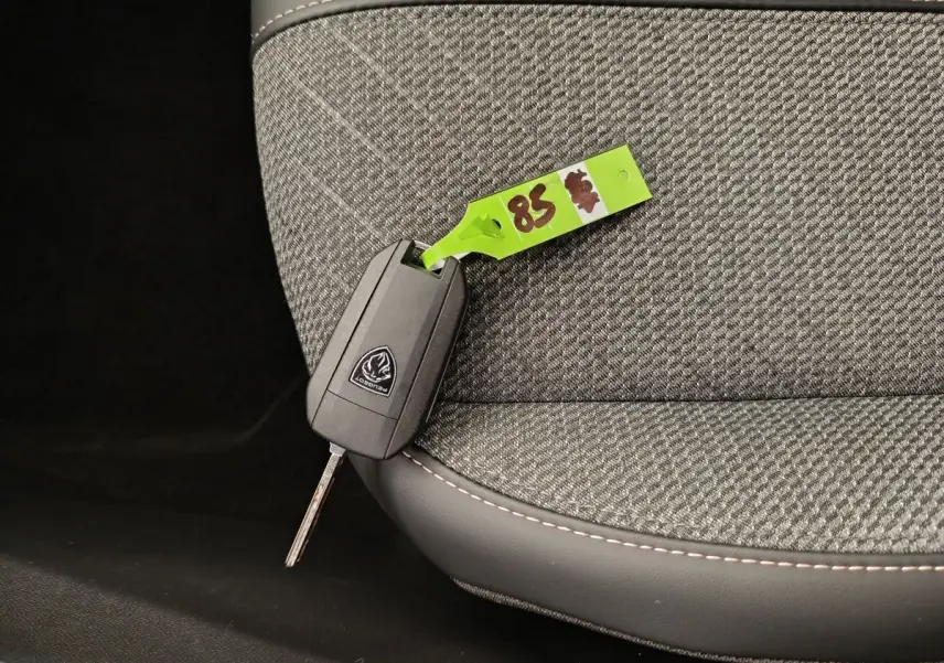 Clé de voiture Peugeot posée sur un siège tissu gris clair avec surpiqûres blanches, intérieur du véhicule visible.