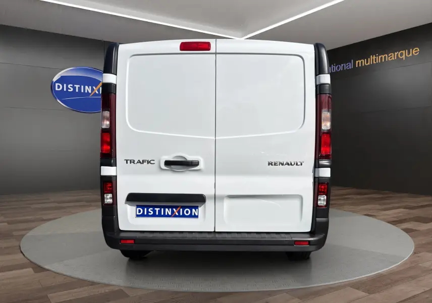 Vue arrière d’un Renault Trafic Fourgon blanc avec portes battantes et feux arrière verticaux visibles.