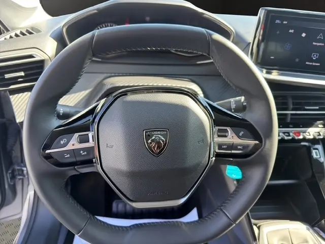 Vue rapprochée du volant cuir multifonctions de la Peugeot 208 gris clair, avec tableau de bord et écran tactile en arrière-plan.