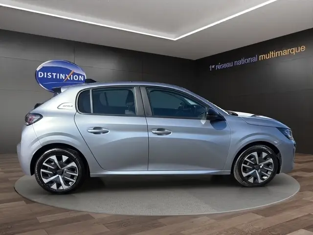 Profil droit d’une Peugeot 208 Style 100 ch gris clair, avec jantes alliage et feux arrière LED visibles en intérieur showroom.