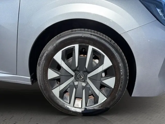 Gros plan sur la roue avant droite d’une Peugeot 208 gris clair, mettant en valeur la jante au design moderne bicolore.