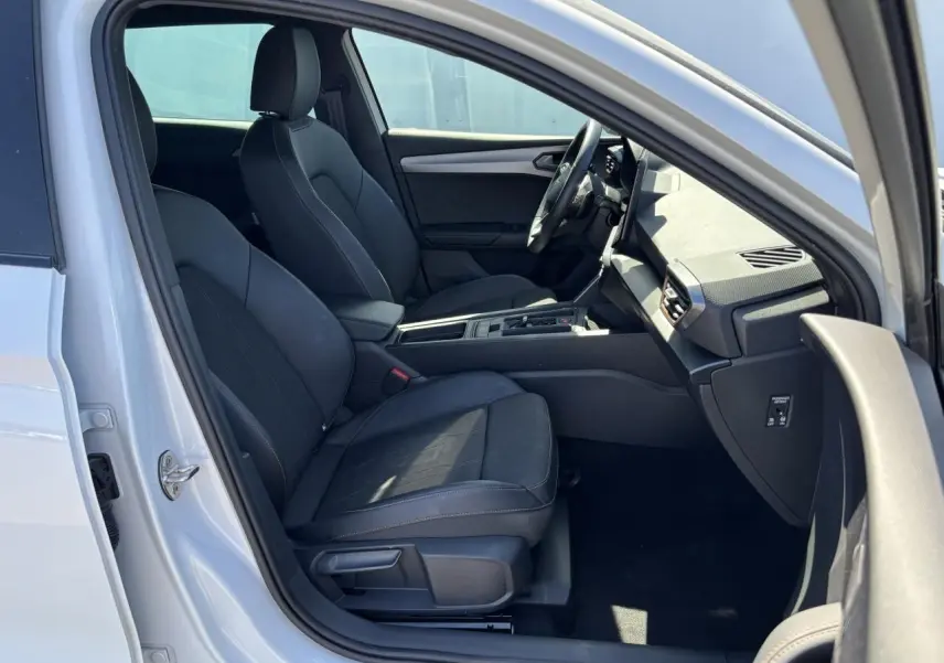 Vue intérieure côté conducteur d'une CUPRA Leon Sportstourer blanche Nevada, sièges noirs et tableau de bord moderne.