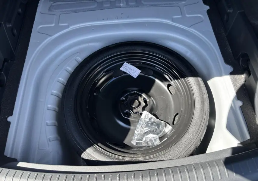 Vue plongeante sur la roue de secours noire dans le coffre blanc Nevada d'une CUPRA Leon Sportstourer 2024.