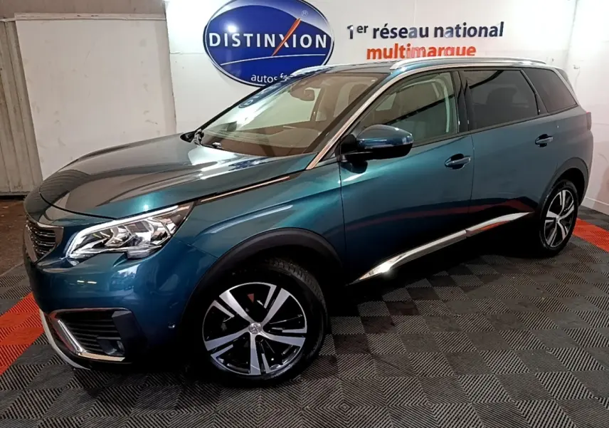 Peugeot 5008 bleu en 3/4 avant droit, avec jantes alliage et calandre distinctive dans un showroom.