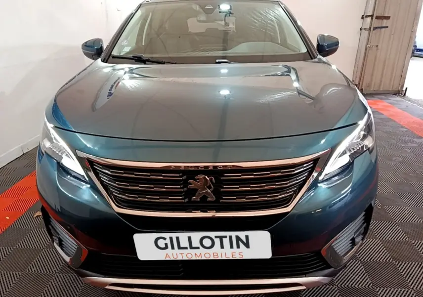 Vue avant d'un Peugeot 5008 bleu métallisé avec calandre chromée et phares LED allumés dans un garage.