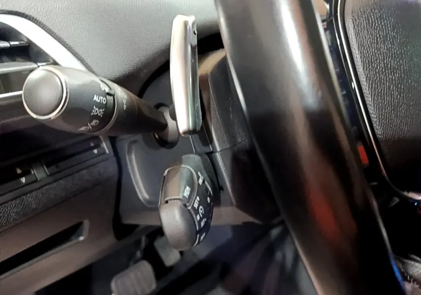 Gros plan sur la colonne de direction et commandes derrière le volant cuir noir du Peugeot 5008 bleu, version 2018.