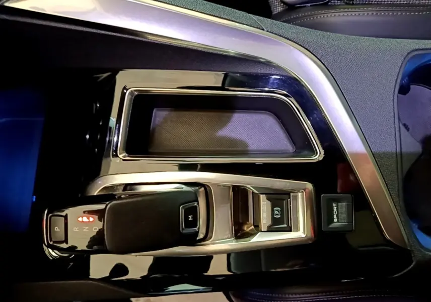 Gros plan sur la console centrale noire brillante du Peugeot 5008 bleu, montrant le levier de boîte automatique et bouton sport.