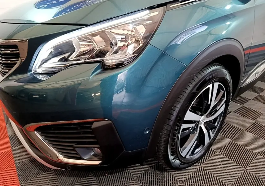 Gros plan sur l'avant droit bleu métallisé du Peugeot 5008 avec phare et jante alliage visible.