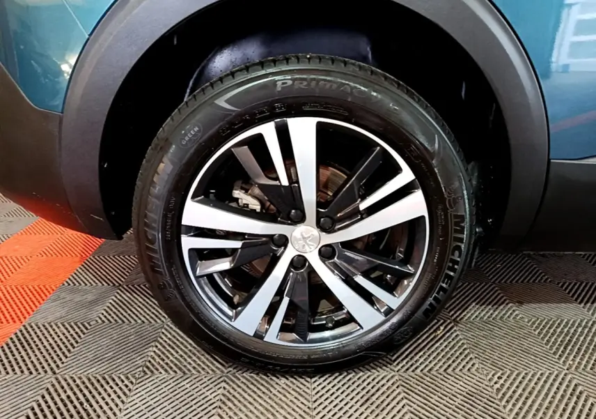 Gros plan sur la roue avant gauche d’un Peugeot 5008 bleu, jante alliage bicolore et pneu Michelin visible.