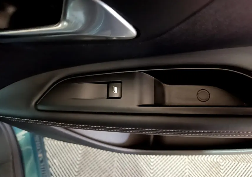 Gros plan sur la commande de lève-vitre côté conducteur en plastique noir avec surpiqûres blanches, intérieur Peugeot 5008 bleu.