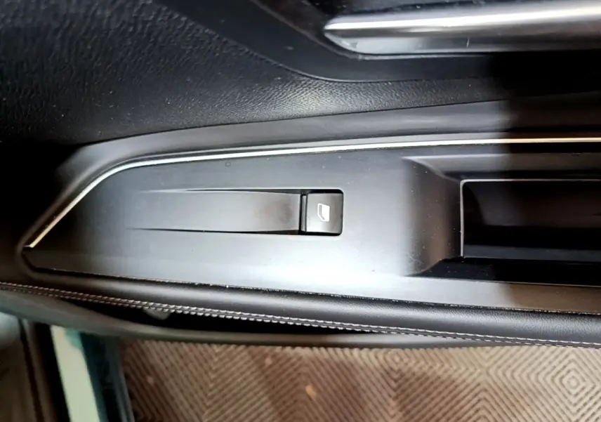Gros plan sur la commande de lève-vitre côté gauche dans l'habitacle noir du Peugeot 5008 bleu 2018.