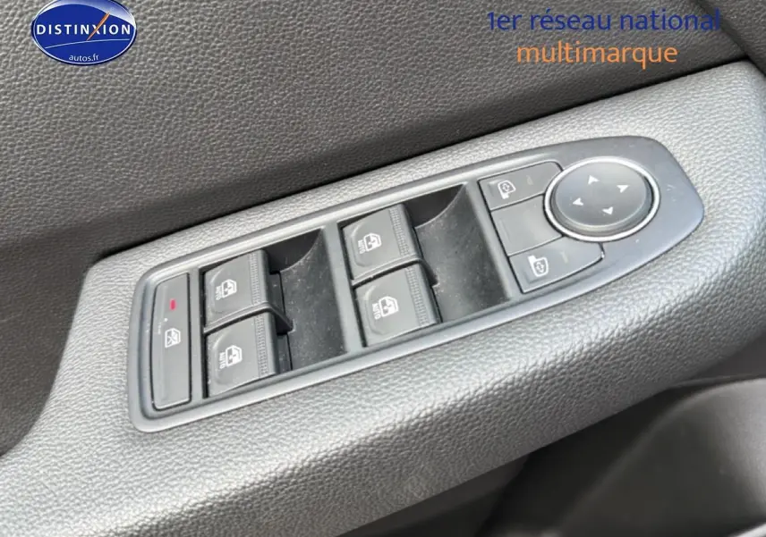 Vue rapprochée des commandes électriques des vitres et des rétroviseurs sur la porte côté conducteur d'une Renault Clio V gris.