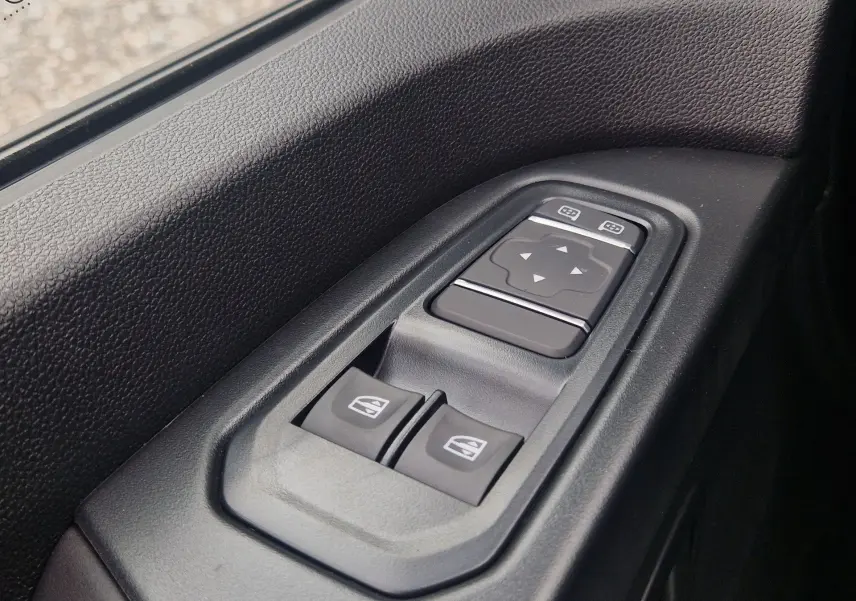 Gros plan sur les commandes de lève-vitres et réglage des rétroviseurs côté conducteur du Renault Trafic Fourgon gris urbain.