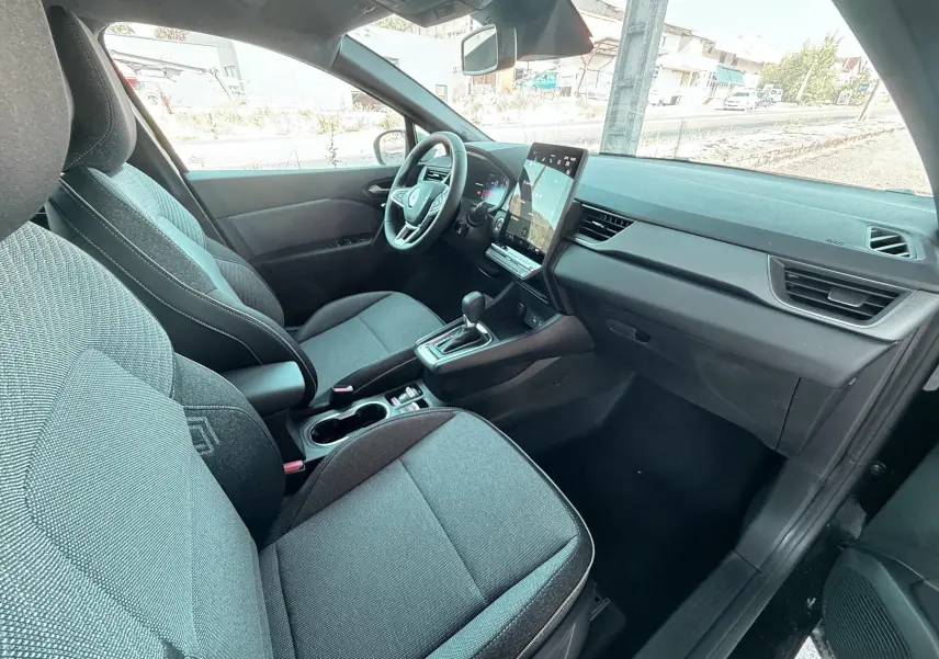Vue intérieure côté conducteur du Renault Captur noir 2025, montrant sièges tissu gris et écran tactile vertical.