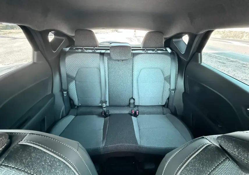Vue intérieure arrière du Renault Captur 2025, sièges tissu gris noir avec ceintures de sécurité visibles.
