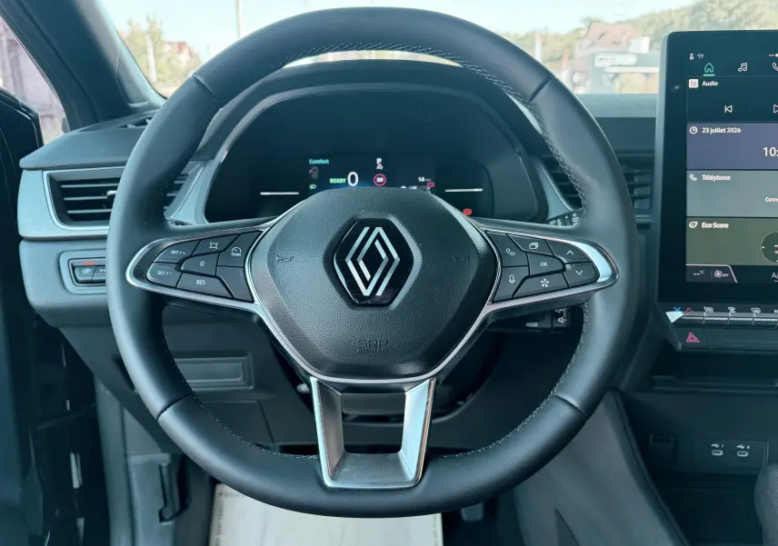 Vue intérieure centrée sur le volant noir de la Renault Captur 2025 avec tableau de bord et écran tactile visible à droite.