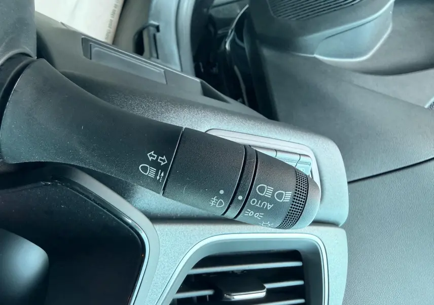 Gros plan sur la commande des feux et clignotants dans l'habitacle gris noir du Renault Captur hybride 2025.