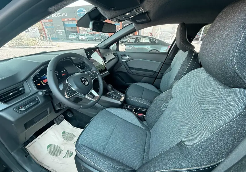 Vue intérieure côté conducteur du Renault Captur 2025, sièges tissu gris noir et tableau de bord moderne.