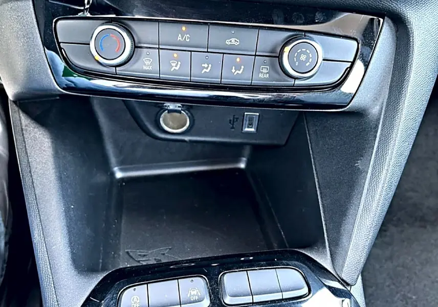 Vue rapprochée de la console centrale noire de l’Opel Corsa 1.2 turbo 100 edition avec commandes clim et prises USB et 12V.