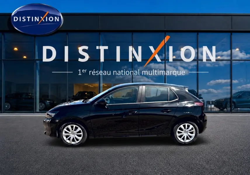 Profil droit d’une Opel Corsa 1.2 turbo 100 edition noire avec enjoliveurs blancs, stationnée devant une vitrine Distinxion.