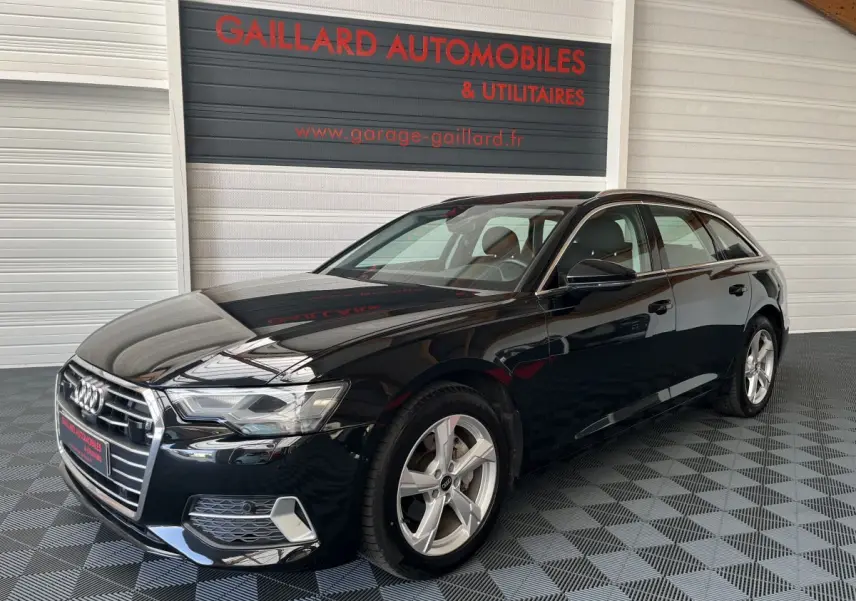 Audi A6 40 TDI S Tronic hybride noire vue 3/4 avant droit dans un showroom avec sol damier gris.