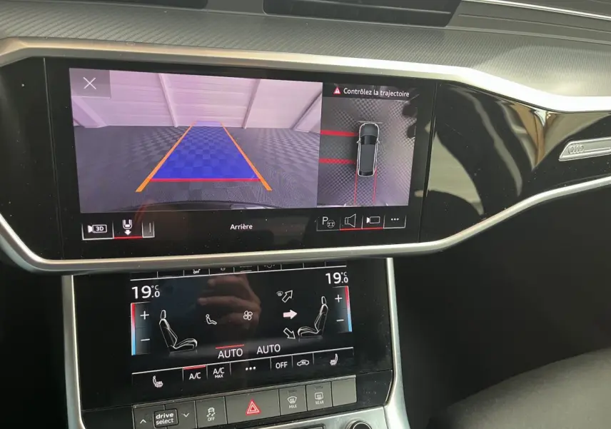 Vue rapprochée du tableau de bord noir d'une Audi A6 40 TDI hybride, écran tactile affichant la caméra de recul et la climatisation.