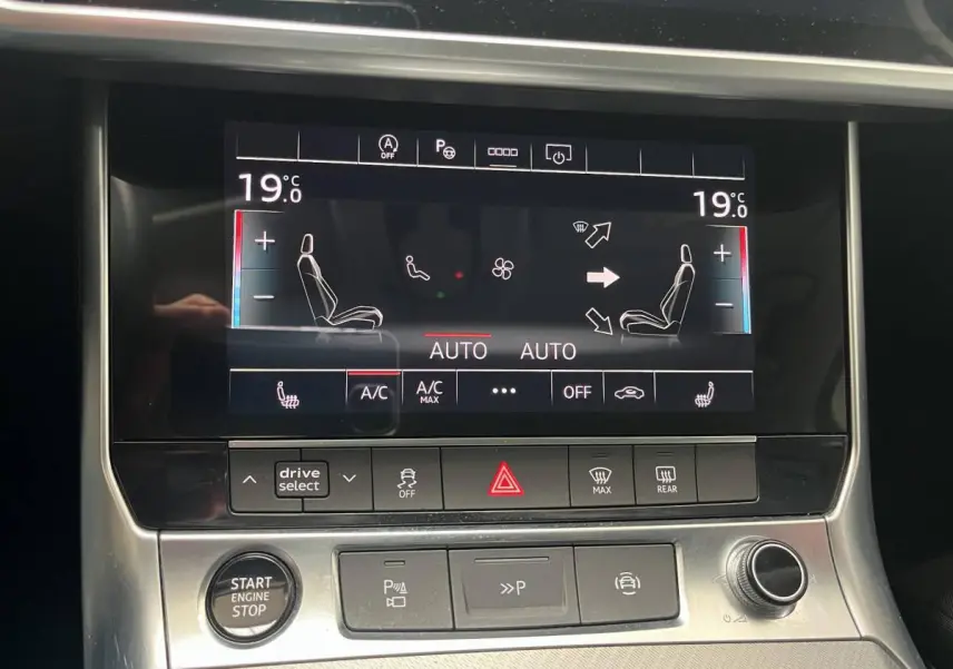 Tableau de bord tactile de l'Audi A6 noir, affichant la climatisation bi-zone à 19°C en vue frontale rapprochée.