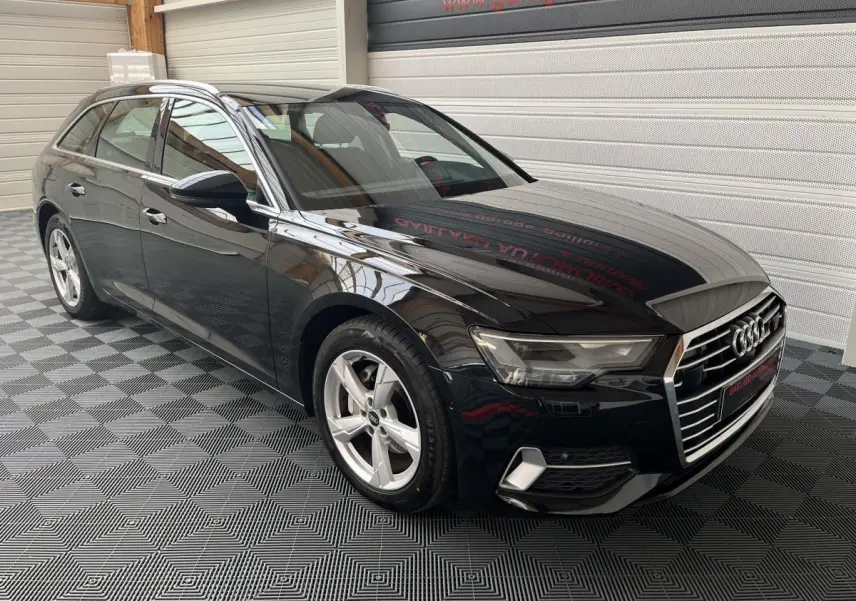 Audi A6 noire vue en 3/4 avant droit dans un garage avec jantes argentées et calandre chromée.