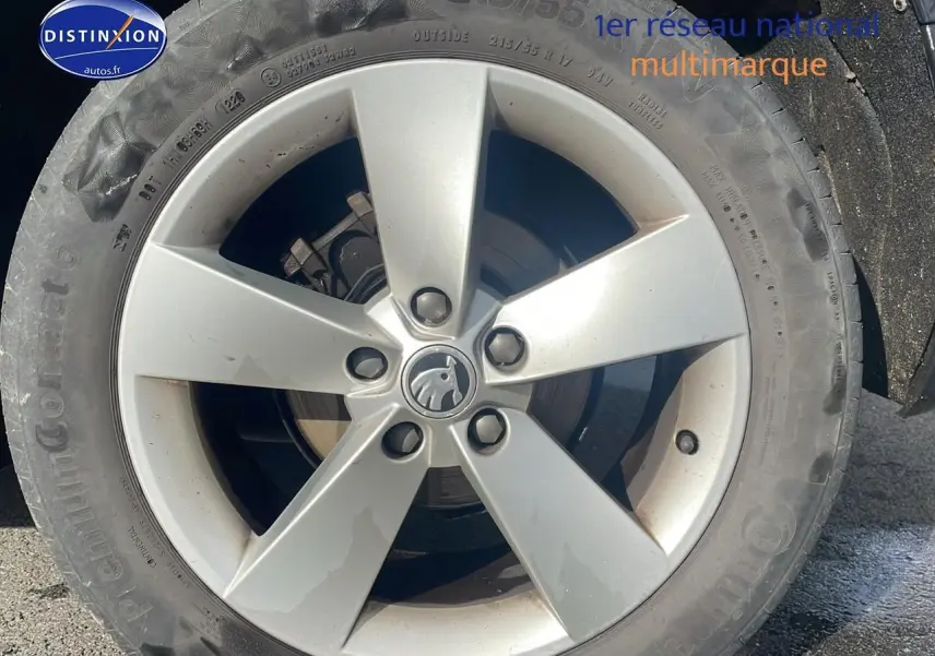 Gros plan sur la jante alu argentée d'une Skoda Karoq noire, mettant en valeur le logo central au soleil.