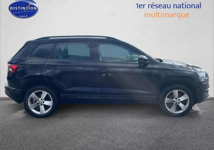 Profil côté gauche d'un SUV SKODA KAROQ noir 2018 avec jantes alu et barres de toit visibles sur fond clair.