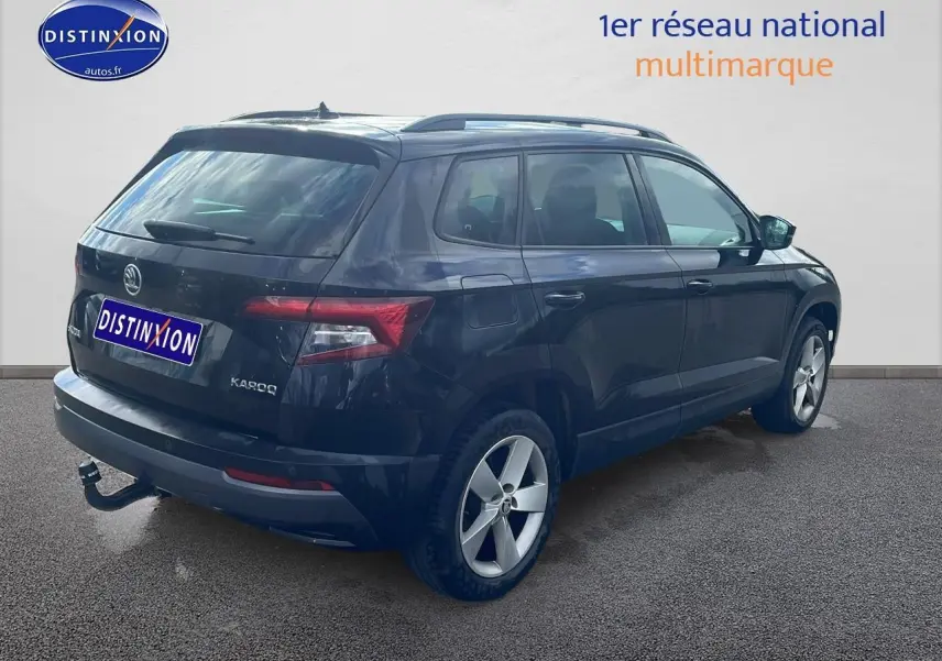 Vue 3/4 arrière droite d'un Skoda Karoq noir avec barres de toit et attelage visible sur un fond neutre.