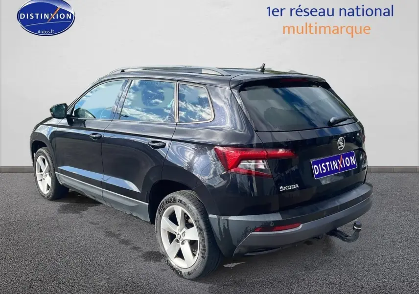 Vue 3/4 arrière droite d'un Skoda Karoq noir avec barres de toit et attelage de remorque visible.