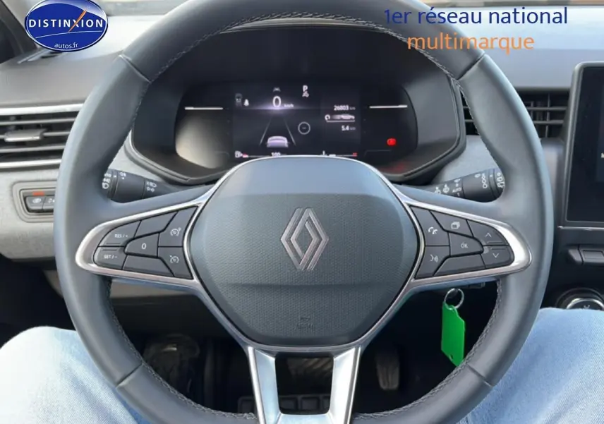 Vue rapprochée du volant multifonction noir de la Renault Clio V avec tableau de bord numérique en arrière-plan.