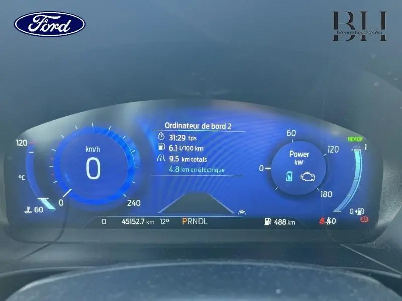 Tableau de bord numérique bleu du Ford Kuga 2023 affichant vitesse, consommation et autonomie électrique.