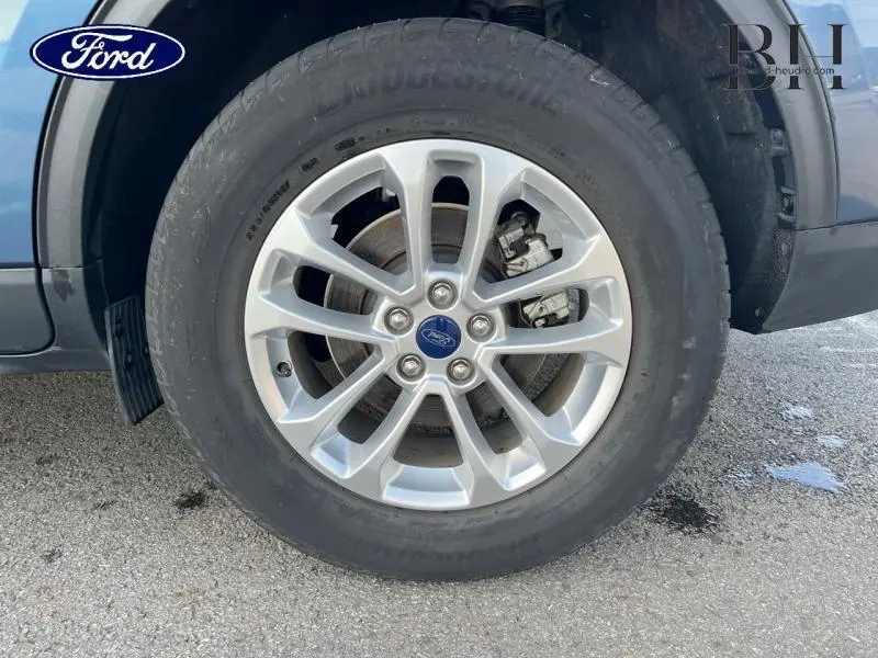 Gros plan sur la roue avant gauche du Ford Kuga bleu azur métallisé avec jante alu et frein à disque visible.