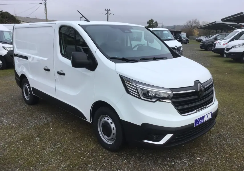 Vue 3/4 avant droit d’un Renault Trafic Fourgon blanc 2025 avec calandre noire et feux LED distinctifs.
