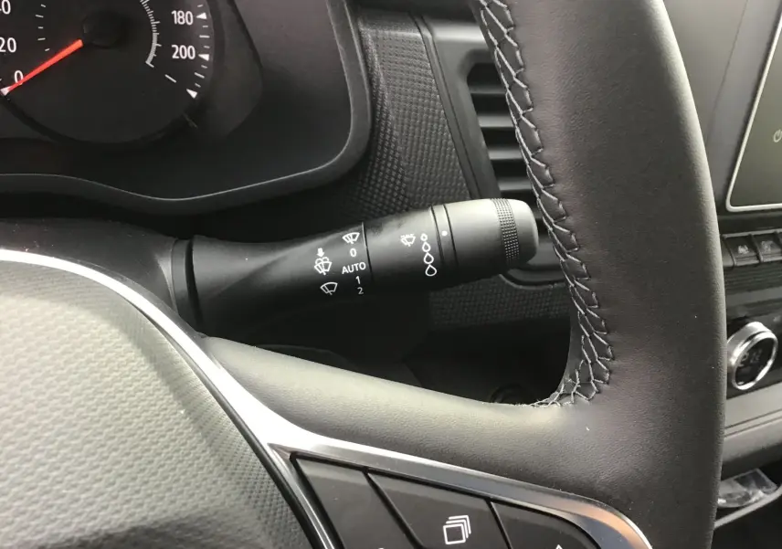 Gros plan sur le volant noir et la commande d’essuie-glace du tableau de bord du Renault Trafic Fourgon blanc.