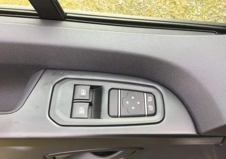 Gros plan sur les commandes de lève-vitres et réglage des rétroviseurs côté gauche du Renault Trafic Fourgon blanc.